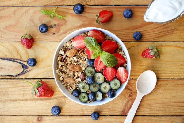 Serving option of granola bowl with mix of nuts, cereals, fruits and berries, greek yogurt. Healthy vegetarian breakfast, organic strawberry, blueberry, mint, almond. Close up, top view, background.