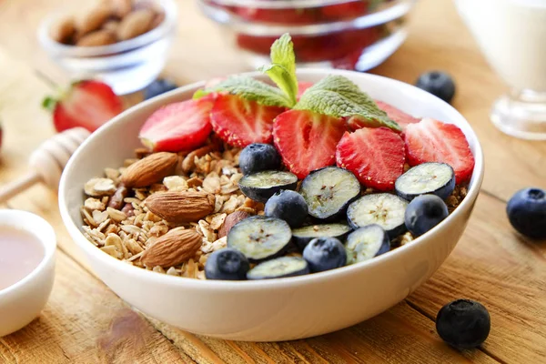 Serving option of granola bowl with mix of nuts, cereals, fruits and berries, greek yogurt. Healthy vegetarian breakfast, organic strawberry, blueberry, mint, almond. Close up, top view, background.