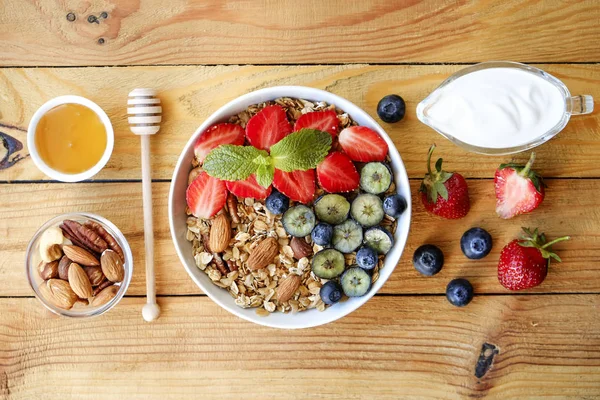 Serving option of granola bowl with mix of nuts, cereals, fruits and berries, greek yogurt. Healthy vegetarian breakfast, organic strawberry, blueberry, mint, almond. Close up, top view, background.