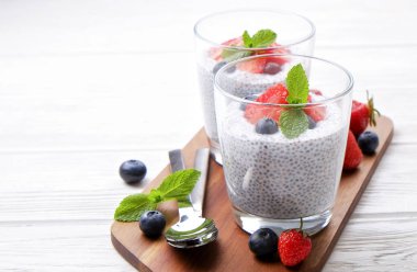 Chia muhallebi vegan badem sütü, nane, yaban mersini ve çilek ile iki porsiyon bardaklarda servis. Sağlıklı vejetaryen kahvaltı, tohum, çilek, Yunan yoğurt, kaşık. Arka plan, yakın çekim, görünümü ana sayfa.