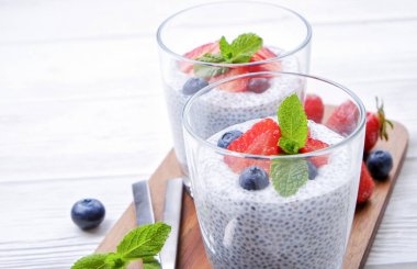 Chia muhallebi vegan badem sütü, nane, yaban mersini ve çilek ile iki porsiyon bardaklarda servis. Sağlıklı vejetaryen kahvaltı, tohum, çilek, Yunan yoğurt, kaşık. Arka plan, yakın çekim, görünümü ana sayfa.