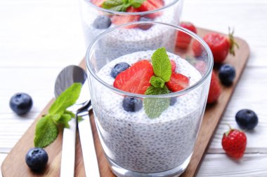 Chia muhallebi vegan badem sütü, nane, yaban mersini ve çilek ile iki porsiyon bardaklarda servis. Sağlıklı vejetaryen kahvaltı, tohum, çilek, Yunan yoğurt, kaşık. Arka plan, yakın çekim, görünümü ana sayfa.