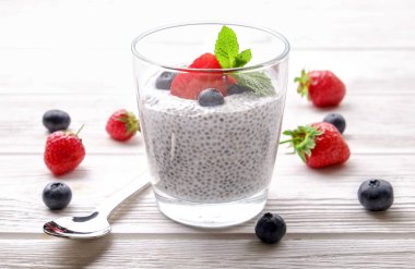 Vegan badem sütü, böğürtlen ve çilek, nane, chia puding bardakta servis bölümü. Sağlıklı vejetaryen kahvaltı, tohum, çilek, Yunan yoğurt, ahşap masa. Arka plan, yakın çekim, görünümü ana sayfa.