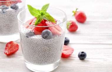 Chia muhallebi vegan badem sütü, nane, yaban mersini ve çilek ile iki porsiyon bardaklarda servis. Sağlıklı vejetaryen kahvaltı, tohum, çilek, Yunan yoğurt, kaşık. Arka plan, yakın çekim, görünümü ana sayfa.