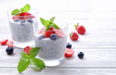 Chia muhallebi vegan badem sütü, nane, yaban mersini ve çilek ile iki porsiyon bardaklarda servis. Sağlıklı vejetaryen kahvaltı, tohum, çilek, Yunan yoğurt, kaşık. Arka plan, yakın çekim, görünümü ana sayfa.