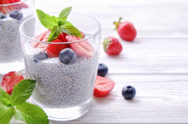 Chia muhallebi vegan badem sütü, nane, yaban mersini ve çilek ile iki porsiyon bardaklarda servis. Sağlıklı vejetaryen kahvaltı, tohum, çilek, Yunan yoğurt, kaşık. Arka plan, yakın çekim, görünümü ana sayfa.