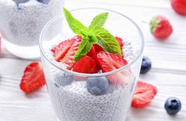 Chia muhallebi vegan badem sütü, nane, yaban mersini ve çilek ile iki porsiyon bardaklarda servis. Sağlıklı vejetaryen kahvaltı, tohum, çilek, Yunan yoğurt, kaşık. Arka plan, yakın çekim, görünümü ana sayfa.