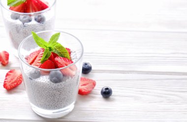 Chia muhallebi vegan badem sütü, nane, yaban mersini ve çilek ile iki porsiyon bardaklarda servis. Sağlıklı vejetaryen kahvaltı, tohum, çilek, Yunan yoğurt, kaşık. Arka plan, yakın çekim, görünümü ana sayfa.