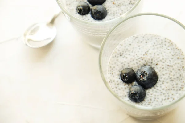 Two portions of chia pudding with vegan almond milk, blueberry, served in glasses. Healthy vegetarian breakfast, seeds, berries & greek yogurt, silver spoon. Background, copy space, close up, top view