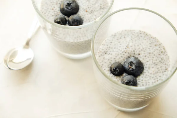 Two portions of chia pudding with vegan almond milk, blueberry, served in glasses. Healthy vegetarian breakfast, seeds, berries & greek yogurt, silver spoon. Background, copy space, close up, top view