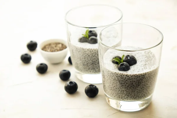 Two portions of chia pudding with vegan almond milk, blueberry & seeds on the side, served in glasses. Healthy vegetarian breakfast, berries & greek yogurt, spoon. Background, copy space, close up.