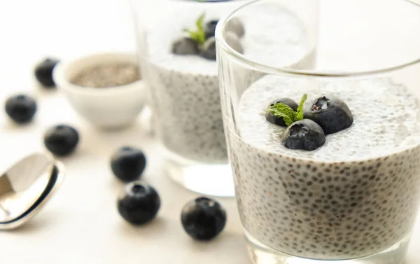 Two portions of chia pudding with vegan almond milk, blueberry & seeds on the side, served in glasses. Healthy vegetarian breakfast, berries & greek yogurt, spoon. Background, copy space, close up.