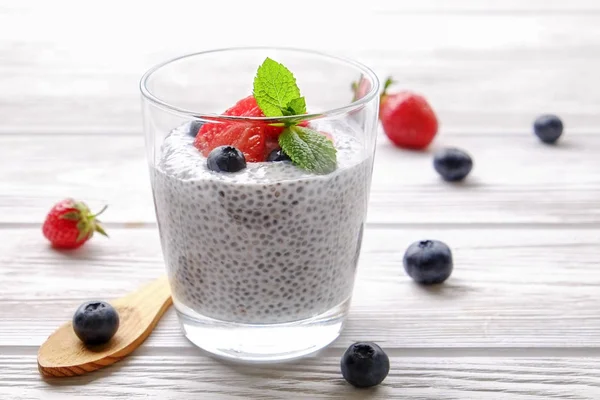 Portion of chia pudding with vegan almond milk, blueberry & strawberry, mint, served in glass. Healthy vegetarian breakfast, seeds, berries, greek yogurt, wooden table. Background, close up, top view.