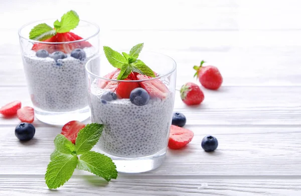 Two portions of chia pudding with vegan almond milk, blueberry & strawberry, mint, served in glasses. Healthy vegetarian breakfast, seeds, berries, greek yogurt, spoon. Background, close up, top view.