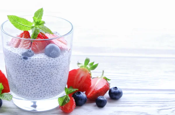 Portion of chia pudding with vegan almond milk, blueberry & strawberry, mint, served in glass. Healthy vegetarian breakfast, seeds, berries, greek yogurt, wooden table. Background, close up, top view.