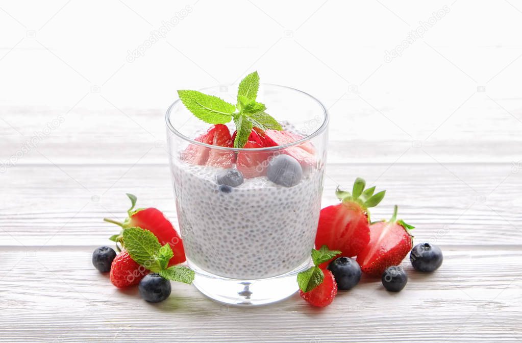 Portion of chia pudding with vegan almond milk, blueberry & strawberry, mint, served in glass. Healthy vegetarian breakfast, seeds, berries, greek yogurt, wooden table. Background, close up, top view.