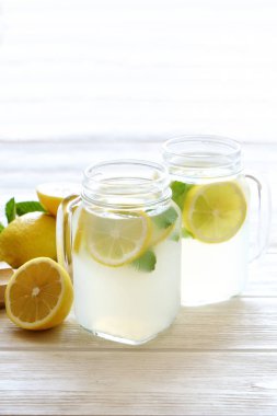 Ev yapımı ferahlatıcı limonata iki mason kavanoza bardak organik olgun limon, bütün ve yarıya, meyva suyu sıkacağı, karıştırma çubuğu, Sıkacağı rustik beyaz ahşap zemin üzerinde dilim. Yakın çekim, görünümü, kopya alanı top