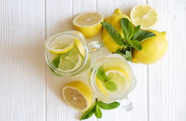Ev yapımı ferahlatıcı limonata iki mason kavanoza bardak organik olgun limon, bütün ve yarıya, meyva suyu sıkacağı, karıştırma çubuğu, Sıkacağı rustik beyaz ahşap zemin üzerinde dilim. Yakın çekim, görünümü, kopya alanı top