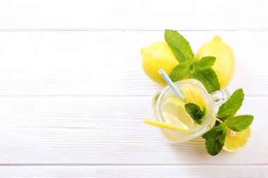 Organik olgun limon, bütün ve yarıya dilim bir mason kavanoza cam canlandırıcı ev yapımı limonata. Alkolsüz içecek rustik beyaz ahşap zemin üzerinde. Yakın çekim, görünümü, kopya alanı top.