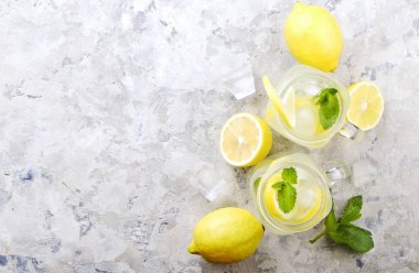 Ev yapımı ferahlatıcı limonata iki mason kavanoza bardak organik olgun limon, bütün ve yarıya, nane, Ice cube grunged gri beton tablo arka plan üzerinde dilim. Yakın çekim, görünümü, kopya alanı top.