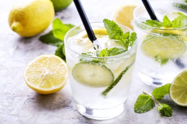 Serinletici alkolsüz mojito limonata içmek organik limon, limon dilimleri, iki kadeh yaprakları, saman, buz küpleri grunged gri beton tablo arka plan üzerine nane. Yakın çekim, görünümü, kopya alanı top.