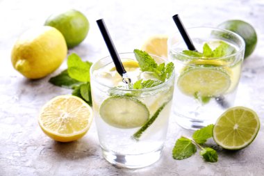 Serinletici alkolsüz mojito limonata içmek organik limon, limon dilimleri, iki kadeh yaprakları, saman, buz küpleri grunged gri beton tablo arka plan üzerine nane. Yakın çekim, görünümü, kopya alanı top.