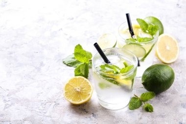 Serinletici alkolsüz mojito limonata içmek organik limon, limon dilimleri, iki kadeh yaprakları, saman, buz küpleri grunged gri beton tablo arka plan üzerine nane. Yakın çekim, görünümü, kopya alanı top.