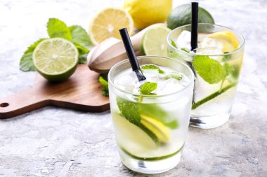 Serinletici alkolsüz mojito limonata içmek organik limon, limon dilimleri, iki kadeh yaprakları, saman, buz küpleri grunged gri beton tablo arka plan üzerine nane. Yakın çekim, görünümü, kopya alanı top.