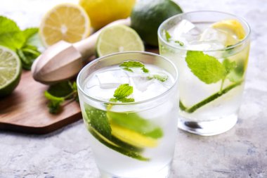 Serinletici alkolsüz mojito limonata içmek organik limon, limon dilimleri, iki kadeh yaprakları, saman, buz küpleri grunged gri beton tablo arka plan üzerine nane. Yakın çekim, görünümü, kopya alanı top.