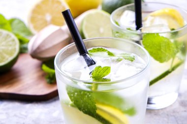Serinletici alkolsüz mojito limonata içmek organik limon, limon dilimleri, iki kadeh yaprakları, saman, buz küpleri grunged gri beton tablo arka plan üzerine nane. Yakın çekim, görünümü, kopya alanı top.