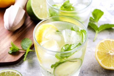 Serinletici alkolsüz mojito limonata içmek organik limon, limon dilimleri, iki kadeh yaprakları, saman, buz küpleri grunged gri beton tablo arka plan üzerine nane. Yakın çekim, görünümü, kopya alanı top.