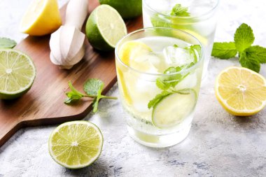Serinletici alkolsüz mojito limonata içmek organik limon, limon dilimleri, iki kadeh yaprakları, saman, buz küpleri grunged gri beton tablo arka plan üzerine nane. Yakın çekim, görünümü, kopya alanı top.
