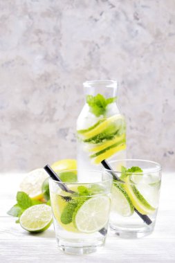 Vintage iki bardak serinletici alkolsüz mojito limonata içki şişesiyle dilimleri ile limon, limon, nane yaprakları, saman, buz üzerinde ahşap masa, beton arka plan. Yakın çekim, görünümü, kopya alanı top.