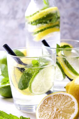 Vintage iki bardak serinletici alkolsüz mojito limonata içki şişesiyle dilimleri ile limon, limon, nane yaprakları, saman, buz üzerinde ahşap masa, beton arka plan. Yakın çekim, görünümü, kopya alanı top.