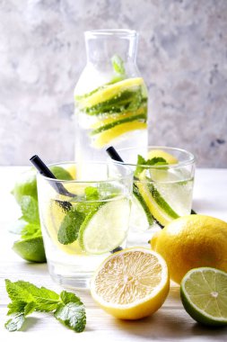 Vintage iki bardak serinletici alkolsüz mojito limonata içki şişesiyle dilimleri ile limon, limon, nane yaprakları, saman, buz üzerinde ahşap masa, beton arka plan. Yakın çekim, görünümü, kopya alanı top.