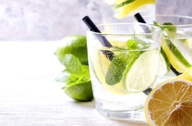 Vintage iki bardak serinletici alkolsüz mojito limonata içki şişesiyle dilimleri ile limon, limon, nane yaprakları, saman, buz üzerinde ahşap masa, beton arka plan. Yakın çekim, görünümü, kopya alanı top.