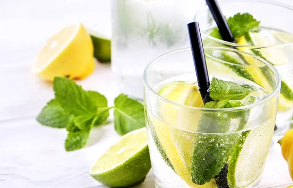 Vintage bottle with two glasses of refreshing non alcoholic mojito lemonade, sparkling water drink with lemon, lime slices, mint leaves, straw, wooden table background. Close up, top view, copy space.