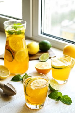 Buzlu limonata sürahi ve iki bardak, ahşap meyve sıkacağı, soğuk narenciye infüzyon su, limon ve limon, nane yaprakları, kesme tahtası üzerinde beyaz ahşap pencere. Daire pencere arka plan, yakın çekim, kopya alanı.