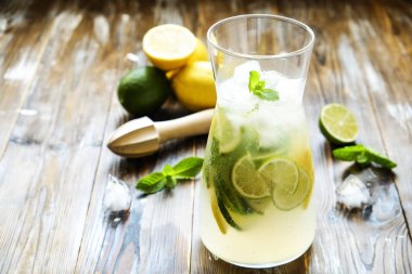 Buzlu limonata sürahi, ahşap meyve sıkacağı, soğuk narenciye infüzyon su içecek limon ve kireç dilimleri, nane yaprakları kahverengi grunged Ahşap dokulu masa güneşli grunged arka plan ile. Yakın çekim, alanı Kopyala.