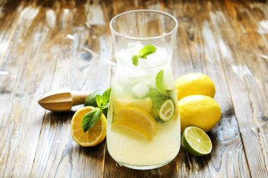 Buzlu limonata sürahi, ahşap meyve sıkacağı, soğuk narenciye infüzyon su içecek limon ve kireç dilimleri, nane yaprakları kahverengi grunged Ahşap dokulu masa güneşli grunged arka plan ile. Yakın çekim, alanı Kopyala.