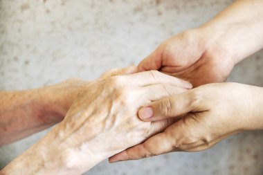 Yaşlı olgun kadın bakım tesisi hastane personel hemşire yardım alır. Üst düzey kadın w / yaşlı kırışık cilt ve bakım verici ellerini kapatın. Büyük anne günlük yaşam. Arka plan, kopya alanı.