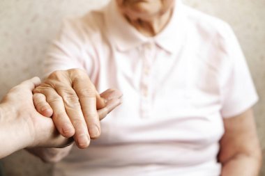 Yaşlı olgun kadın bakım tesisi hastane personel hemşire yardım alır. Üst düzey kadın w / yaşlı kırışık cilt ve bakım verici ellerini kapatın. Büyük anne günlük yaşam. Arka plan, kopya alanı.