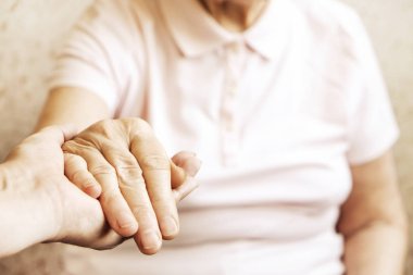 Yaşlı olgun kadın bakım tesisi hastane personel hemşire yardım alır. Üst düzey kadın w / yaşlı kırışık cilt ve bakım verici ellerini kapatın. Büyük anne günlük yaşam. Arka plan, kopya alanı.