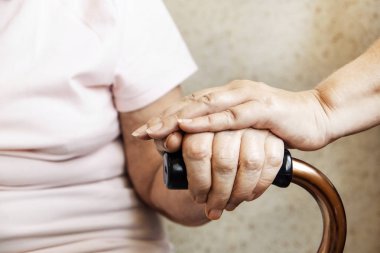 ' Yaşlı çift baston sapı tutan üst düzey kadın fecility iyi bak. Hastane bakım evinde, baston ile oturma rahatlatıcı olgun erkek hemşire. Arka plan, w / kırışık cilt eller üzerinde Kapat.