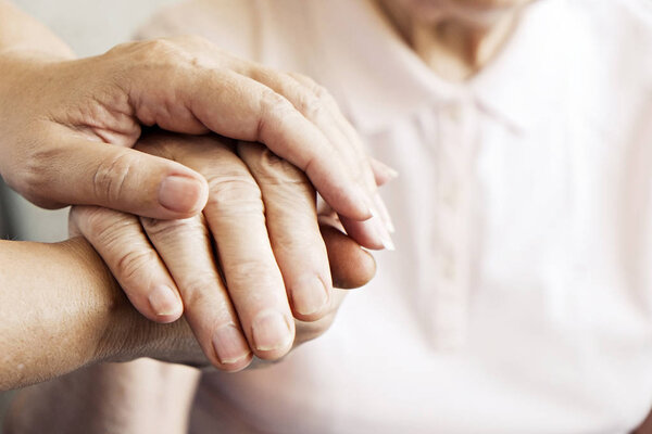 Mature female in elderly care facility gets help from hospital personnel nurse. Senior woman w/ aged wrinkled skin & care giver, hands close up. Grand mother everyday life. Background, copy space.