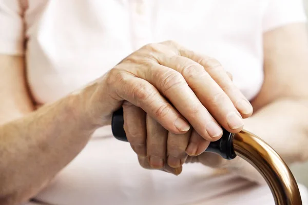 Elderly woman in nursing home, wrinkled hand with clearly visible veins holding walking quad cane. Old age senior lady arms with freckles lay on aid stick handle bar. Background, close up, copy space.