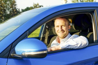 Direksiyon simidi, onun yeni Karayip Mavisi sürüş test araba oturan genç yakışıklı bir iş adamı. Aracını, gülümseyen adam newely satın alınan otomobil ile memnun. Portre, yakın çekim, arka plan