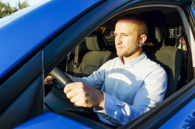 Direksiyon simidi, onun yeni Karayip Mavisi sürüş test araba oturan genç yakışıklı bir iş adamı. Aracını, gülümseyen adam newely satın alınan otomobil ile memnun. Portre, yakın çekim, arka plan