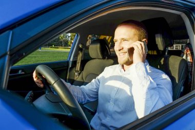 Yeni Karayip mavi arabasına binme direksiyon oturan genç yakışıklı işadamı. Aracın içinde resmi ware giyen adam, sürüş Evet gülümsüyor. Portre, yakın çekim, arka plan.