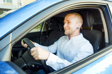 Direksiyon simidi, onun yeni Karayip Mavisi sürüş test araba oturan genç yakışıklı bir iş adamı. Aracını, gülümseyen adam newely satın alınan otomobil ile memnun. Portre, yakın çekim, arka plan